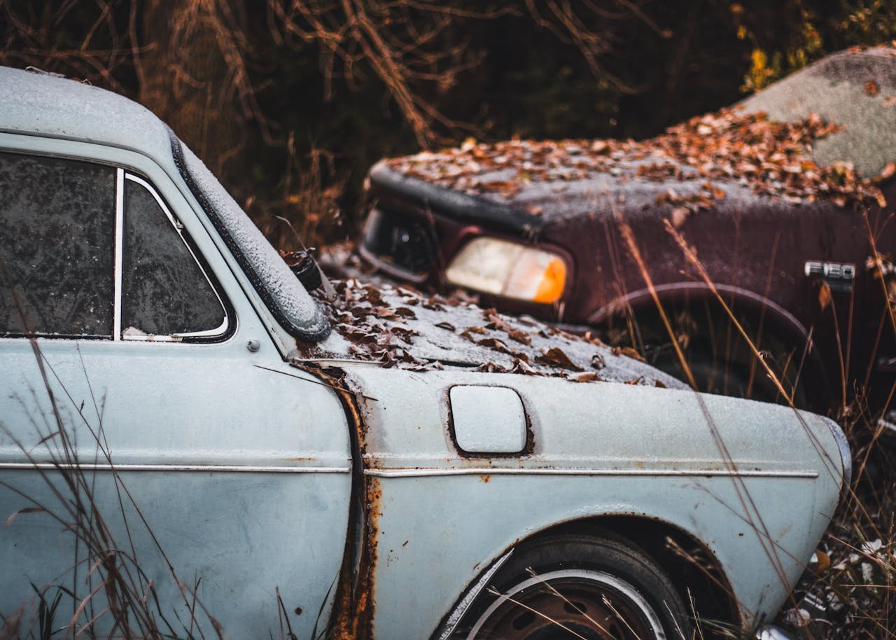 Vintage cars abandoned in rustic junkyard, covered in frost and autumn leaves.